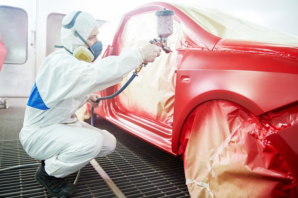Human worker painting car red.